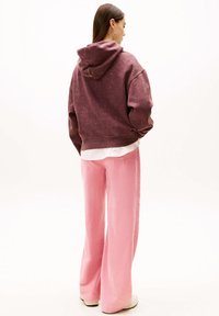 Sweat à capuche surdimensionné bordeaux avec une finition texturée, associé à un pantalon en velours côtelé rose coupe droite. Des baskets de couleur claire complètent le look.