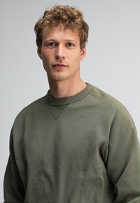 Olijfgroene sweatshirt van zachte stof, met een ronde hals en lange mouwen, een licht gestructureerd oppervlak en ribbelaccenten.