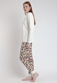 Top de manga larga crema con cuello redondo, combinado con pantalones de pijama multicolores de estampado con personajes de dibujos animados y puños elásticos.