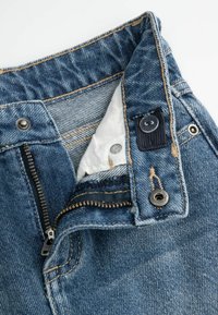 Jeans z denimu z zamkiem błyskawicznym, srebrnymi akcentami i ciemnoniebieskim pasem. Posiadają kontrastową podszewkę oraz detale przeszyć.