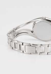 Orologio in acciaio inossidabile argentato con bracciale a maglie lucidato, cassa rotonda e un quadrante liscio e minimalista. Presenta il logo del marchio inciso.
