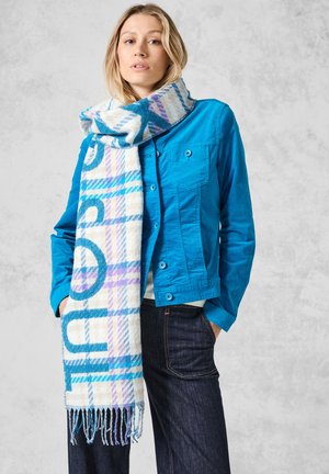 Giacca di denim blu con due tasche sul petto, abbinata a una sciarpa a righe nei colori bianco, blu e viola con motivo a quadri, rifinita con bordi frangiati.