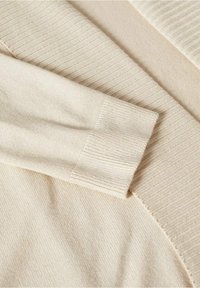 Tissu beige tricoté avec poignets et ourlet côtelés, montrant une texture douce et des détails de couture fins en gros plan.