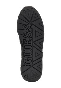 Semelle de chaussure en caoutchouc noir avec motif de grip texturé ; présente un grand logo "GUESS" au centre et des accents triangulaires partout.