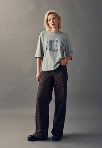 Szary oversize t-shirt z napisem "École de" w niebieskim i czerwonym kolorze; zestawiony z brązowymi spodniami w panterkę o szerokich nogawkach oraz czarnymi butami na platformie.