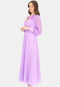 Lawendowa sukienka z długim rękawem i głębokim dekoltem w kształcie litery V, z teksturowanym kwiatowym akcentem na ramieniu, królującym materiałem oraz paskiem w talii. Miękki, lekki materiał.