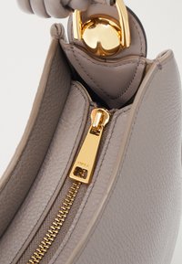 Harmaan nahkalaukun sisäosa, jossa on kultainen vetoketju ja koristeena metalliosia. Huomiota herättävä tekstuuri ja kultainen pyöreä vetimen yksityiskohta.