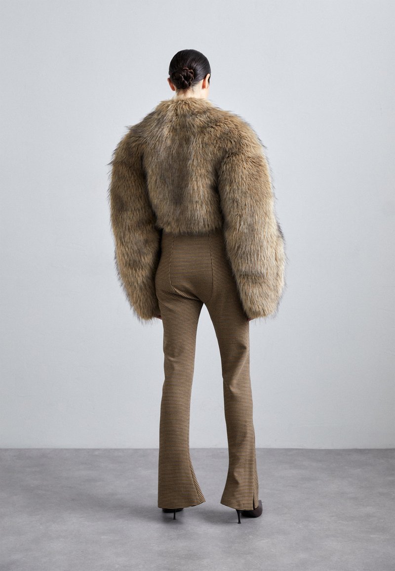 Faux fur brown jacket with oversized sleeves, paired with fitted houndstooth trousers. High heels complete the ensemble.