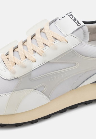 White leather and gray textile sneaker featuring pale beige laces, transparent overlays, and a black rubber sole with notable detailing.