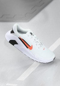 Hvid atletisk sko med mesh-overdel, sorte accenter og en fremtrædende orange swoosh. Sørger for snørebåndsdesign og struktureret sål.