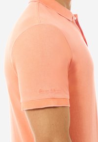 Korallfarbenes Poloshirt aus strukturiertem Material, mit kurzen Ärmeln und Knopfverschluss. Dezentes Logodetail am Ärmel.
