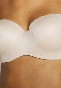 Strapless beige bh met een gladde textuur, gevormde cups en een golvende bovenrand, ontworpen voor naadloos dragen onder kleding.