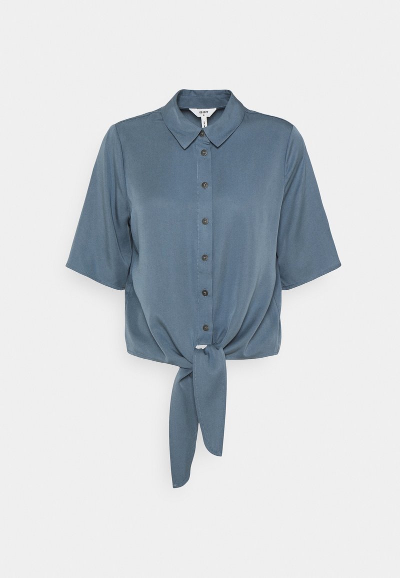 Chemise à manches courtes bleu acier avec col, boutons et nœud à l'avant, présentée sur un fond blanc.