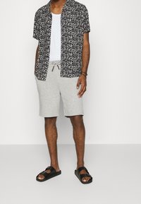 Krátký rukáv triko v černém a šedém leopardím vzoru s volným střihem, doplněné šedými teplákovými šortkami a černými plochými sandály.