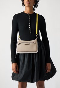 Borsa a tracolla in pelle beige con bordo crema, dotata di una tasca con zip, una tracolla gialla rimovibile e una superficie liscia e texture.