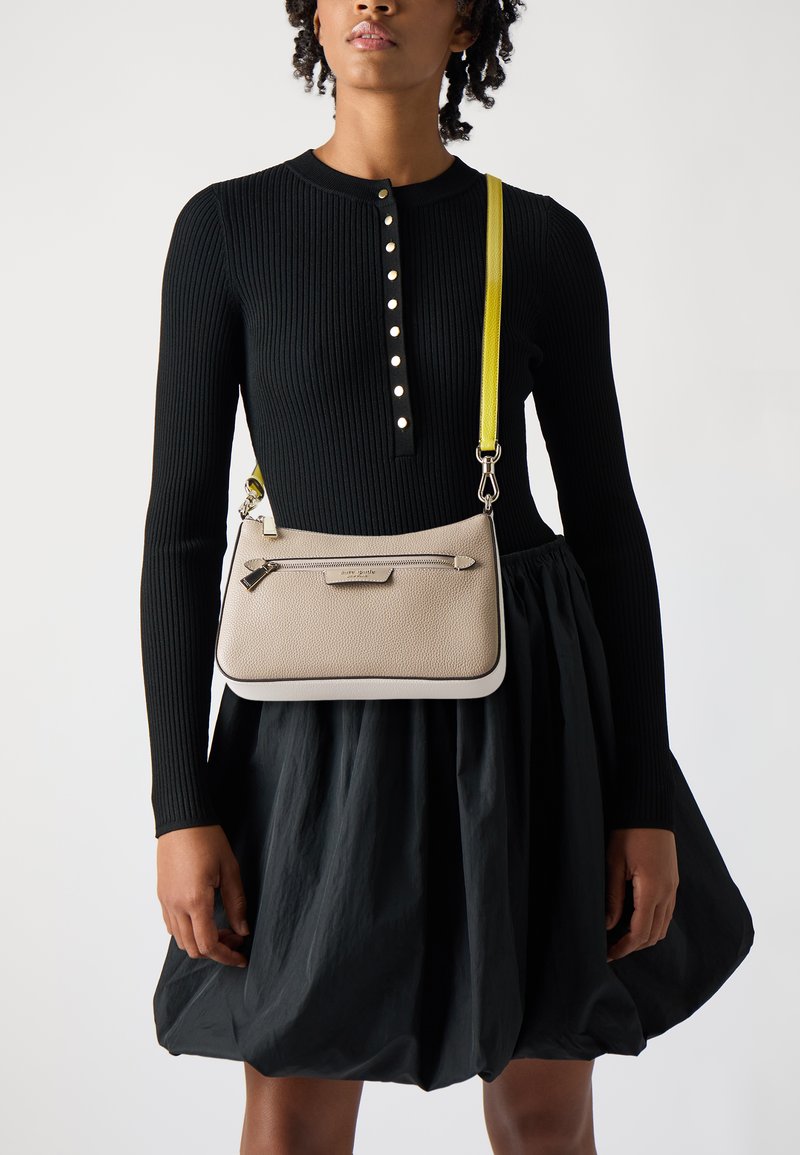 Borsa a tracolla in pelle beige con bordo crema, dotata di una tasca con zip, una tracolla gialla rimovibile e una superficie liscia e texture.