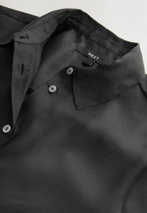 Schwarzes Hemd mit Kragen aus glattem Stoff mit einem subtilen Glanz. Verfügt über Knopfverschlüsse und ein Etikett mit der Aufschrift "NEXT."