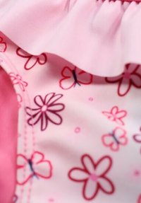 Tissu rose avec un motif floral comportant des fleurs roses et violettes. Le détail froncé le long du bord ajoute de la texture. Matériau globalement lisse.