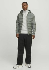Gepolsterte, grau-grüne Jacke mit Kapuze, Reißverschluss vorne, gerippten Bündchen, kombiniert mit schwarzen weiten Hosen und metallischen Sneakers.