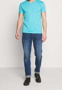 Türkises V-Ausschnitt-T-Shirt mit kurzen Ärmeln, kombiniert mit geraden blauen Jeans und schwarzen Schnürstiefeln mit umgeschlagenem Saum.