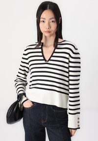 Black and white striped sweater with a V-neck design and ribbed cuffs, featuring three decorative buttons on the sleeve.