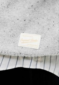 Gros plan d’un vêtement tricoté gris moucheté avec une étiquette rectangulaire blanche portant la mention "Creative Dept Originals Stordir Jack & Jones."