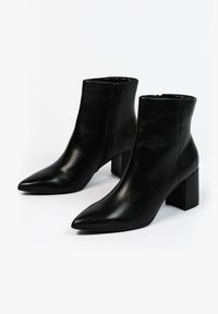 Zwarte leren enkelboots met spitse neuzen, lage blokhakken en ritssluitingen aan de zijkant. Gladde textuur met een subtiele glans.