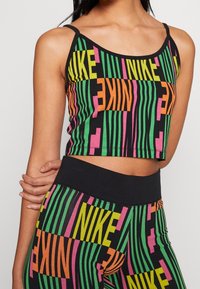Czarny krótki top i legginsy z kolorowym, wyrazistym napisem "NIKE" w zielonym, różowym i pomarańczowym kolorze. Posiada cienkie ramiączka i dopasowany krój.