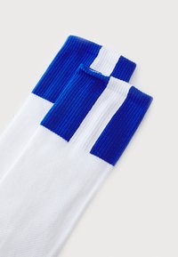 Suknjične nogavice do kolen z rebrasto teksturo. Bele osnove, z modrim vrhom in horizontalnimi belimi črtami. Mehka, elastična tkanina.