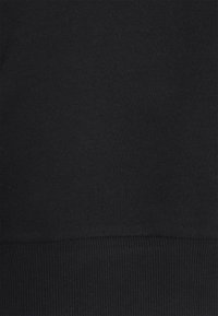 Texture de tissu noir avec un ourlet côtelé en bas, montrant des détails de tricot et une couleur sombre uniforme.