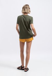 Olijfgroene T-shirt met korte mouwen, gecombineerd met gele shorts, met een relaxed fit en een soepele textuur. Zwarte sandalen maken de look af.