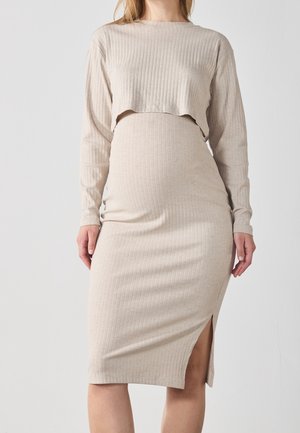 Femme portant une tenue deux pièces beige côtelée avec un top court à manches longues et une jupe ajustée avec une fente latérale.