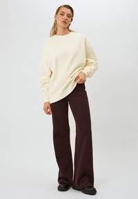 Felpa oversize color crema con polsini a coste abbinata a pantaloni a gamba larga marrone scuro, con dettagli di texture e scarpe nere lisce.