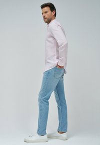 Camisa de manga larga rosa claro con un ajuste relajado, combinada con jeans rectos de color azul claro. El calzado consiste en zapatillas blancas.