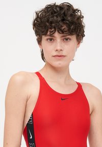 Bañador rojo con acentos laterales negros, con un logo de Nike. Hecho de un material suave y elástico, tiene tirantes finos y un diseño ajustado.