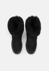 Czarne zamszowe botki z puszystą, przypominającą futro wyściółką, okrągłym noskiem oraz prostą czarną gumową podeszwą. Projekt charakteryzuje się złożonym mankietem.