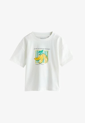 Weißes T-Shirt mit kurzen Ärmeln, bedruckt mit einer Bananengrafik und französischem Text "J'aime les bonnes bananes, J'aime le soleil" vor grün gestreiftem Hintergrund.