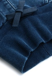 Cintura elastica blu scuro con righe texturizzate, dotata di un fiocco in corda di stoffa. Materiale denim morbido con una finitura liscia.