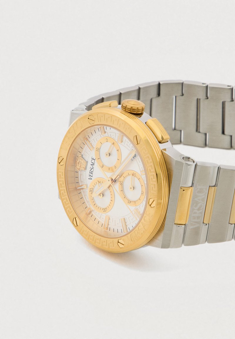 Goldene und silberne Edelstahl-Armbanduhr mit weißem, gemustertem Zifferblatt, drei Hilfszifferblättern und einer strukturierten Lünette, die den Markennamen zeigt.