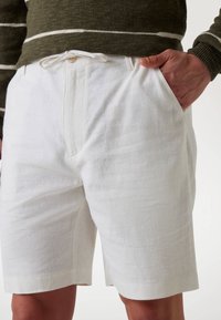 White linen shorts with a straight cut, featuring a drawstring closure and side pockets. Smooth, lightweight texture with minimal stitching details.