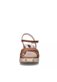 Sandalo in pelle color cuoio con cinturini incrociati, cinturino alla caviglia e suola beige testurizzata con accenti floreali. Tacco piatto, design con punta aperta.