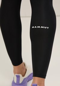 Leggings neri realizzati in tessuto elasticizzato, con il logo bianco "Mammut" sulla coscia. Texture liscia e design aderente.