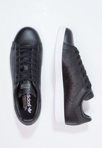 Černé kožené tenisky s texturovaným povrchem, vybavené bílou gumovou podrážkou, šněrovacím designem a logem na jazyku a na straně.