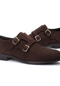 Zapatos de ante marrón con doble hebilla que presentan un diseño de punta redonda y un leve tacón. Acentos de hardware dorado en las correas ajustables.