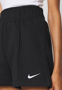 Svarta Nike-shorts med elastisk midja, med en vit logotyp på nederkanten, tillverkade av ett mjukt, texturerat tyg.