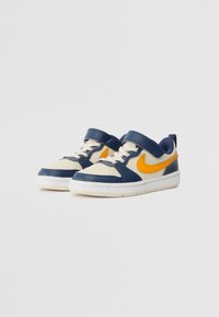 Tennarit, joissa on sininen nahka-yläpinta, kerma värejä ja oranssi Nike-logo. Varustettu tarranauhalla ja rei'itetyllä varpaalla hengittävyyden lisäämiseksi. Kumipohja.