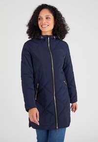 Abrigo acolchado en color navy con capucha, con cierre frontal y dos bolsillos con cremallera, acentuado por detalles en dorado y un patrón de diamantes.