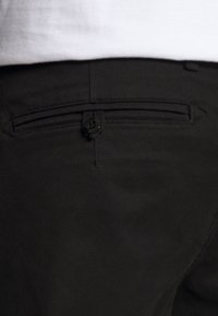 Zwarte katoenen broek met een achterzak met knoopsluiting, subtiele textuur en een rechte pijp.