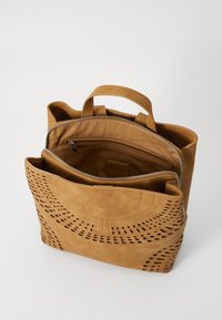 Tannsuede håndveske med utskårne mønstre, doble håndtak og glidelåslommer. Har en jevn tekstur og minimalistisk design.