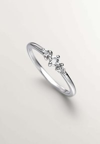 Anillo de plata con tres piedras redondas transparentes en el centro, con una banda lisa y sutiles acentos texturizados alrededor de las piedras.